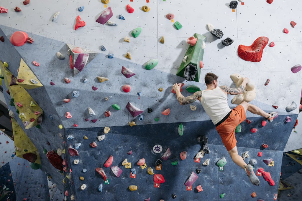 Adult male rock climber scaling a colorful indoor climbing wall, showcasing athleticism and focus in a dynamic setting.